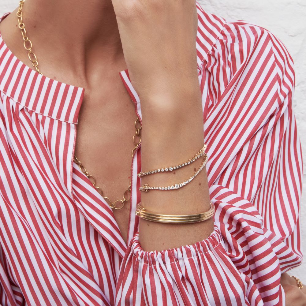 A woman wearing a red and white striped shirt with gold bracelets, including a Rainsun Tennis Bracelet from Ondyn, in graduated sizes pattern.