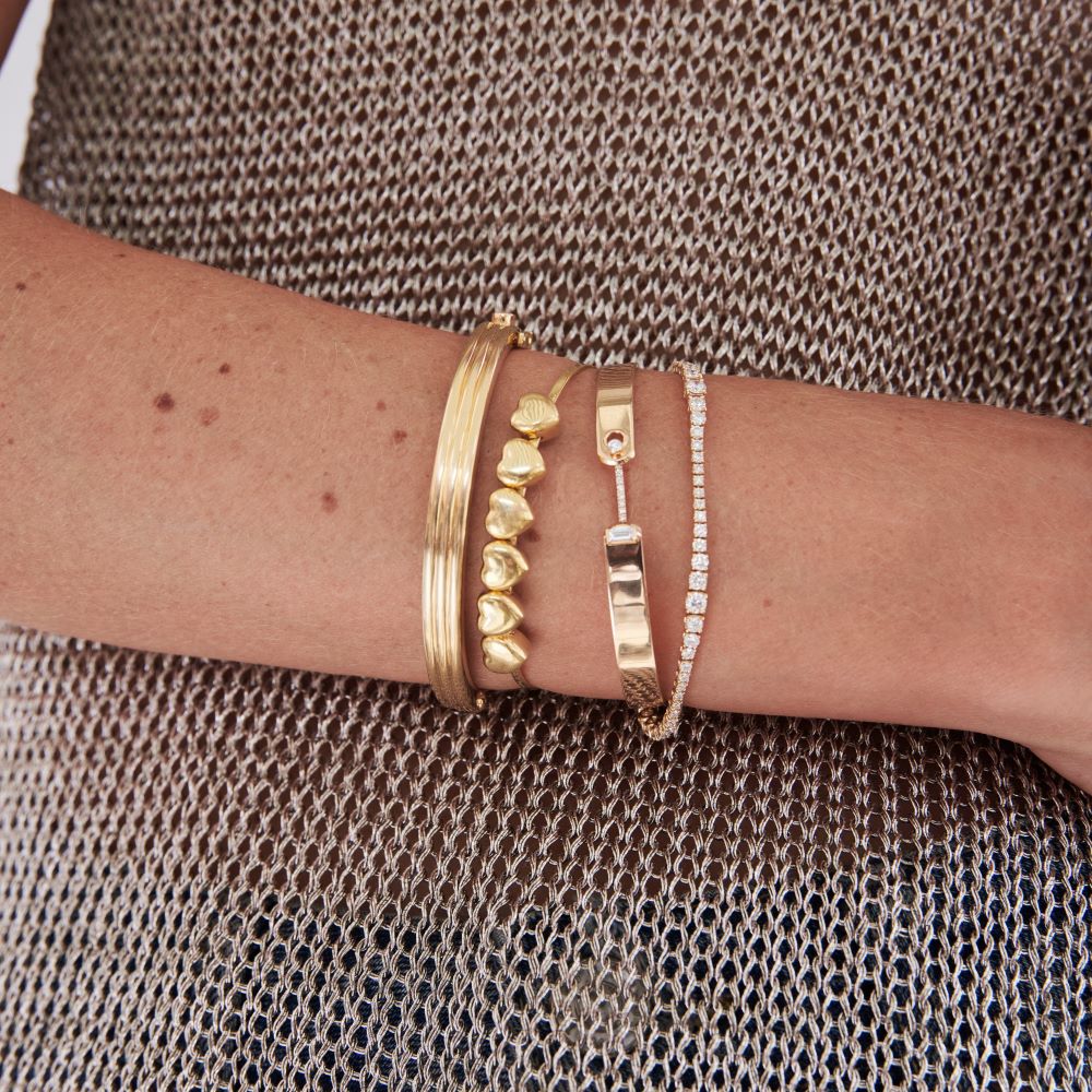 A woman's arm with three Christina Alexiou Heart Bracelets adorned, showcasing a satin finish.