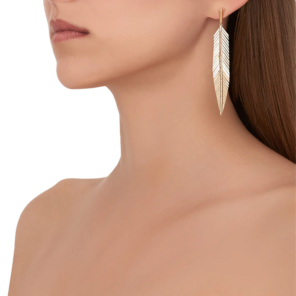 A woman flaunting a pair of Cadar feather drop earrings in 18k yellow gold.