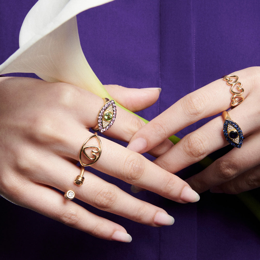A woman's hand holding a Lorraine West Heart Eye Ring with a heart center and a flower.