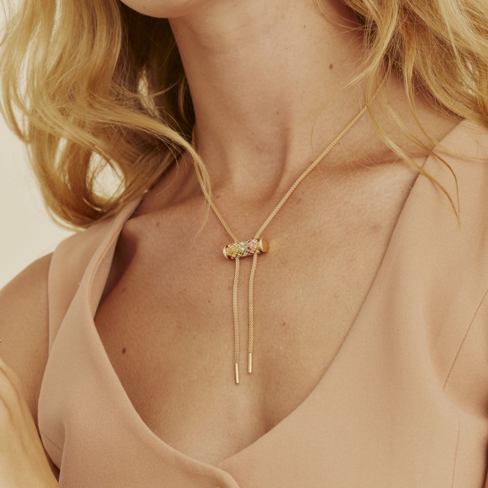 A blonde woman wearing a Nouvel Heritage Latch Chain Yellow Gold Full Diamond Necklace with a gold tassel.