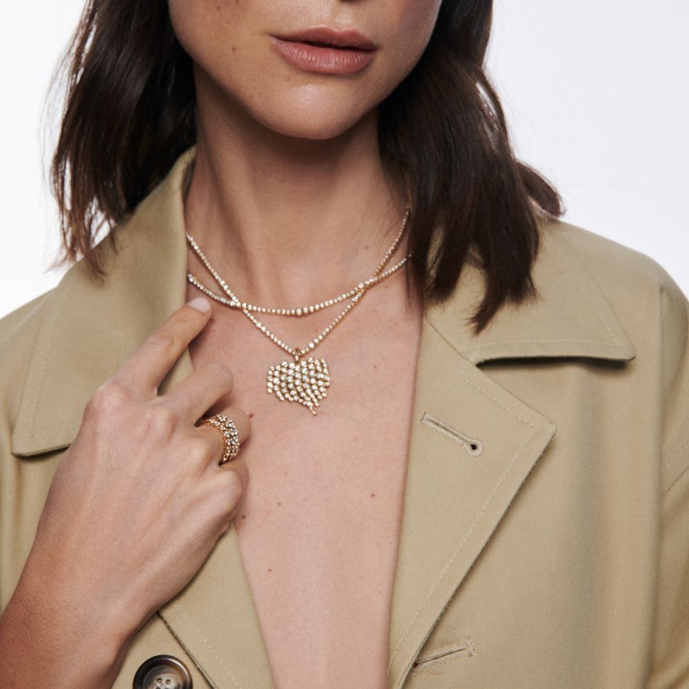 A woman in a tan coat wearing a gold necklace and Ondyn's Diamond Fringe Charm earrings.