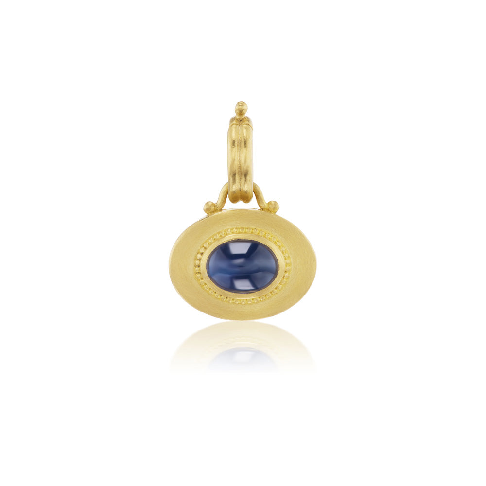 An oval blue sapphire pendant in yellow gold, the Granulated Heart Charm by Prounis.