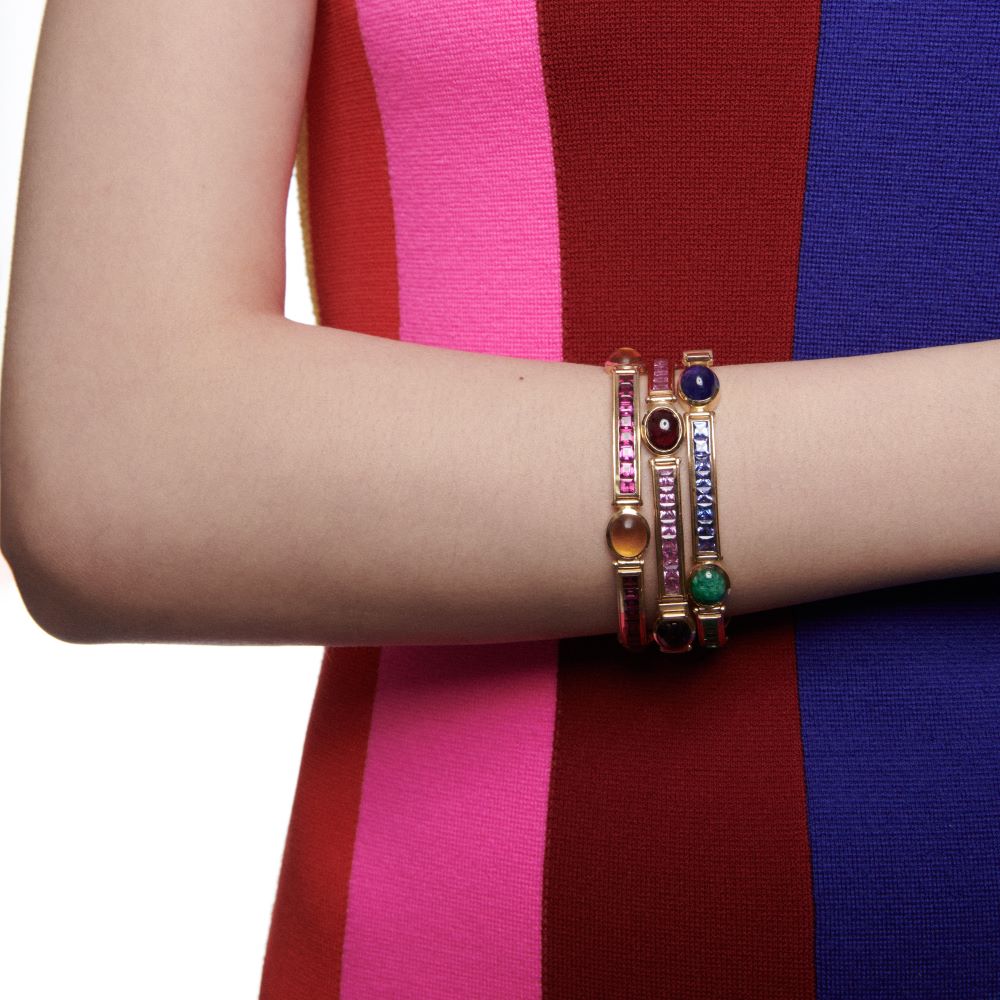 A woman wearing a colorful dress and VAN yellow gold Stack Bracelets adorned with colorful stones.