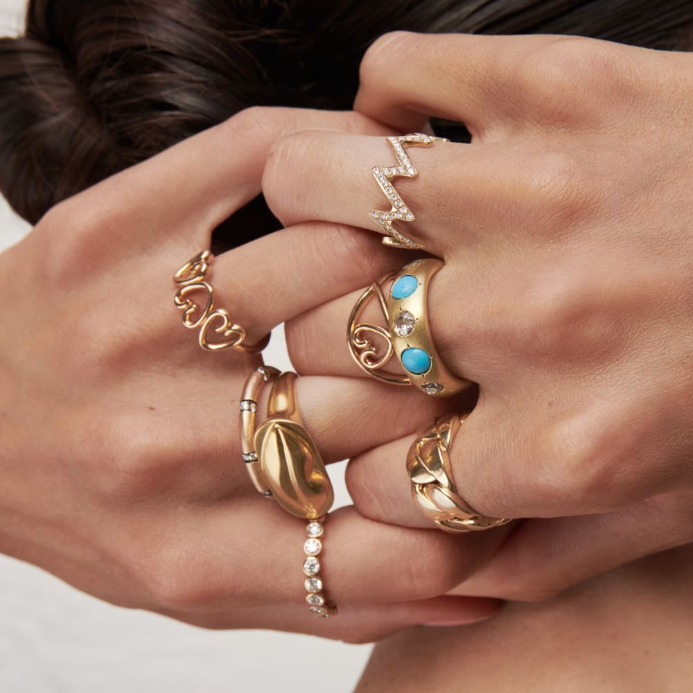 A woman's hands are tenderly holding a Christina Alexiou Kiss Me Tender Ring and a turquoise ring.