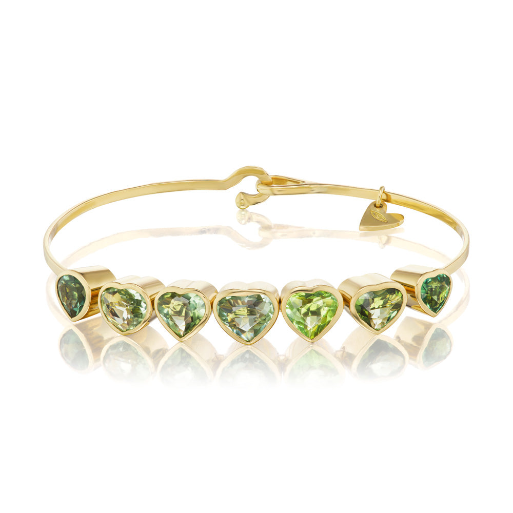 A Christina Alexiou 7 Heart Bracelet with green peridot stones and yellow gold.