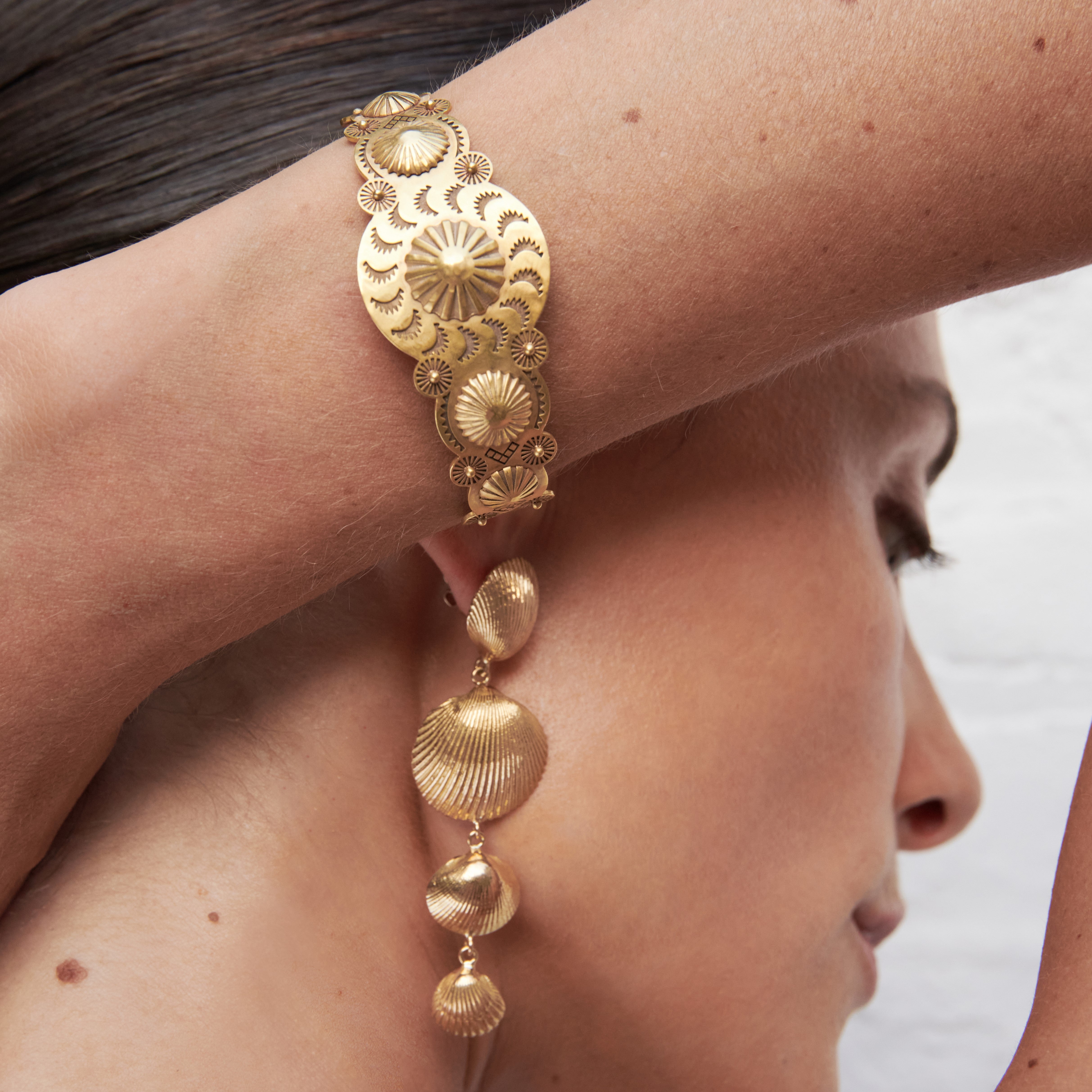 A woman wearing a Cadar yellow gold cuff bracelet and Cadar Four Shell drop earrings.