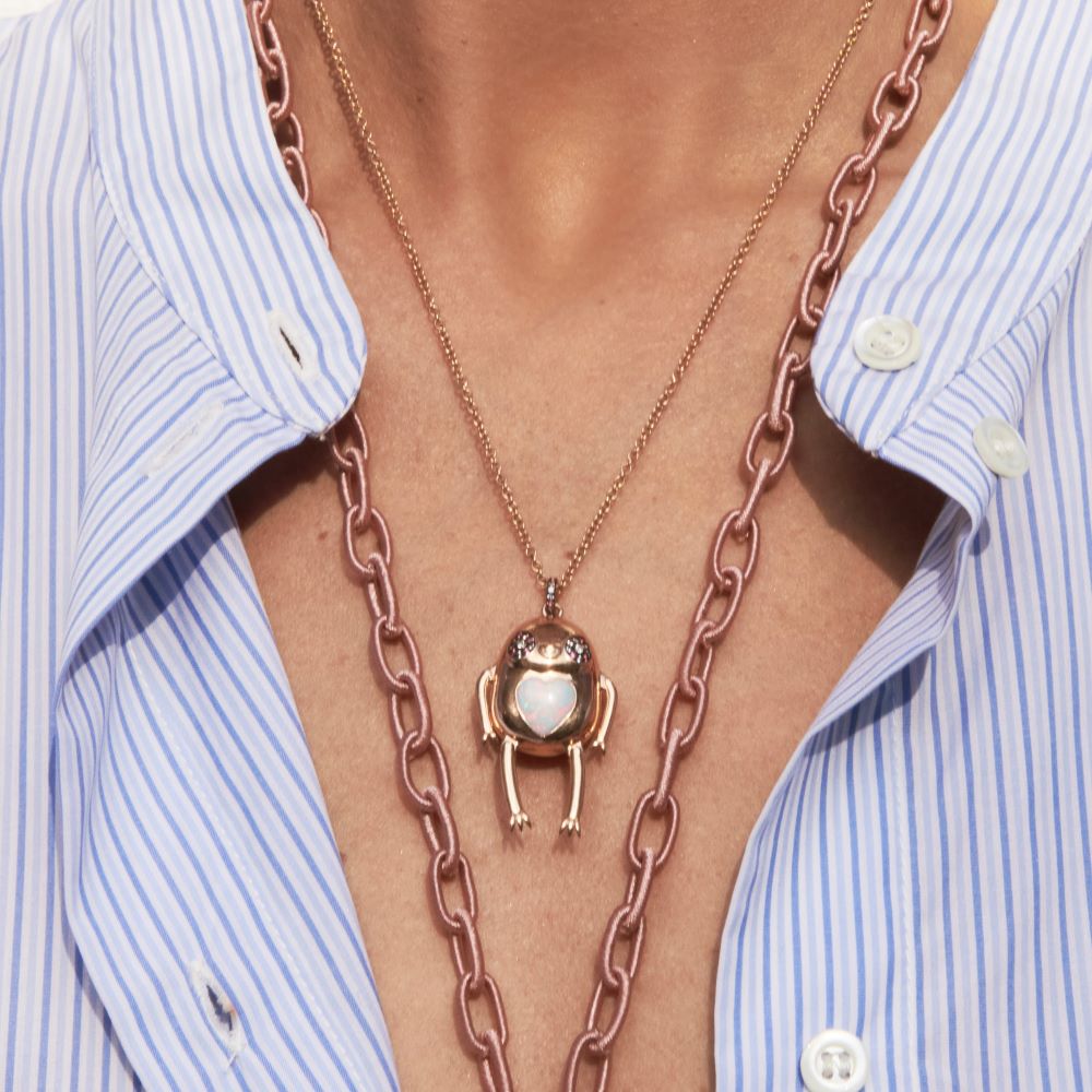 A woman is wearing a Daniela Villegas Sloth Magia Pendant Necklace with an opal heart pendant.