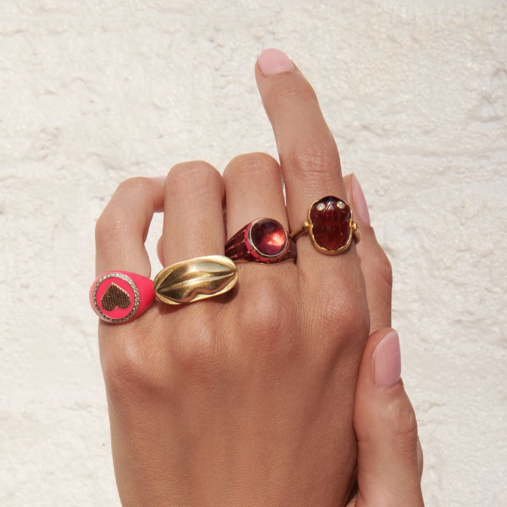 A woman's hand holding a Christina Alexiou Kiss Me Tender Ring with a pink stone.