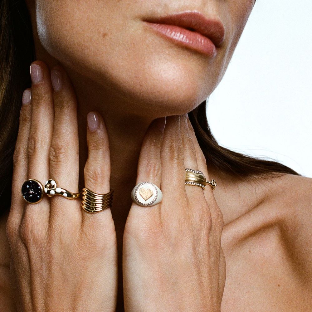 A woman is posing with a KWIT Heart Signet Ring on her hand.