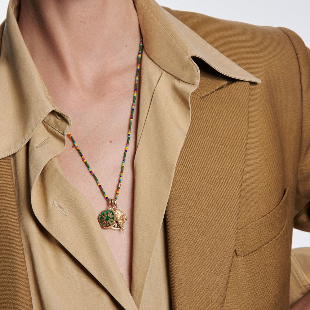 A woman is wearing a tan jacket with a Luis Morais yellow gold necklace featuring the Short Fingers Crossed Charm.