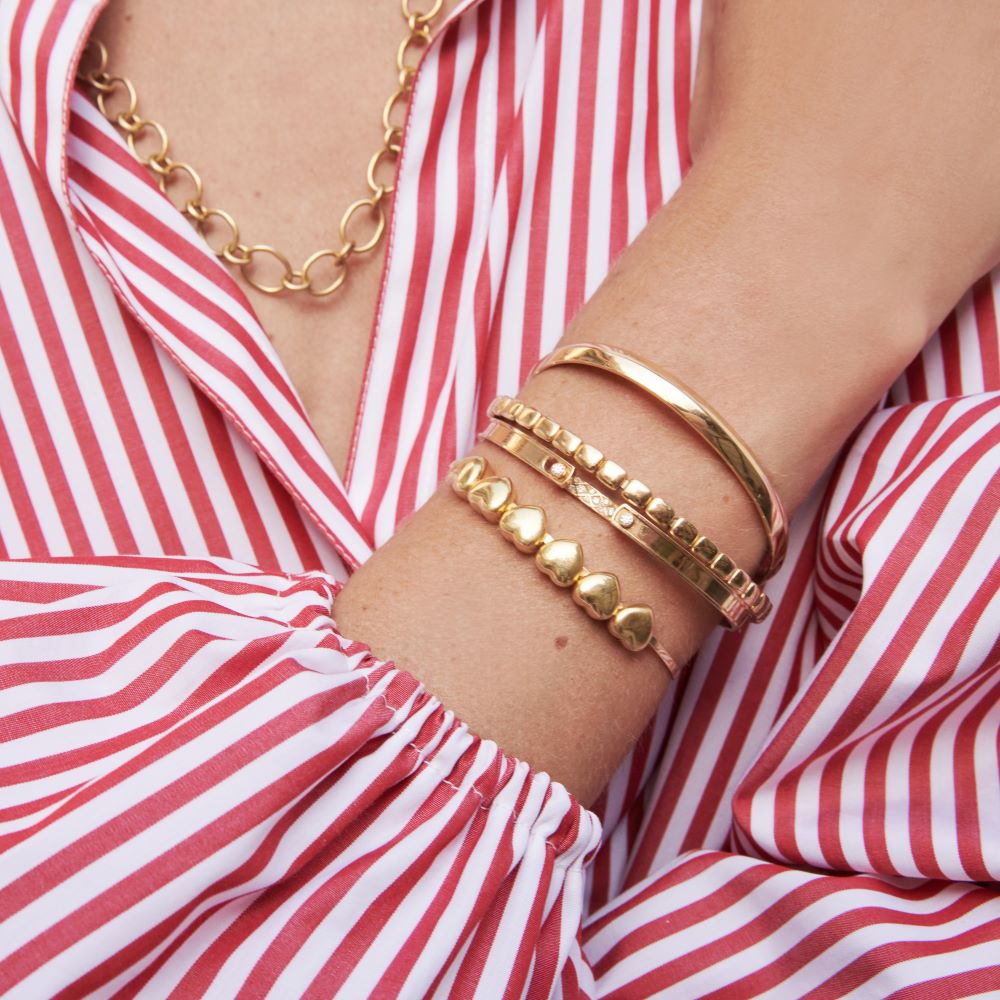 A woman wearing a red and white striped shirt and gold bracelets adorned with round diamonds, including the Nouvel Heritage Parisian Stroll Mood Bangle.