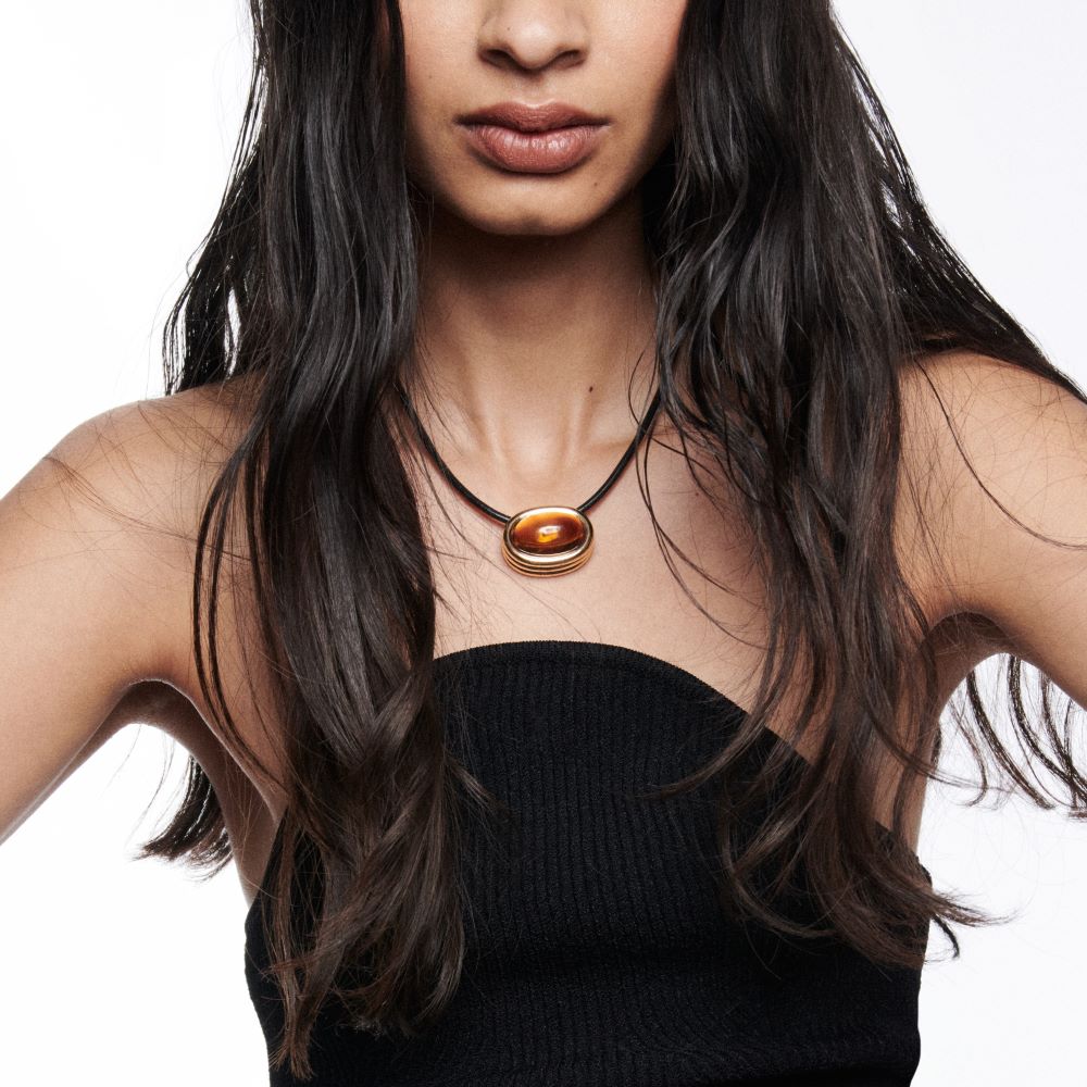 A woman with long dark hair wearing a Beck Scuba Citrine Cabochon Choker Necklace on a leather cord.