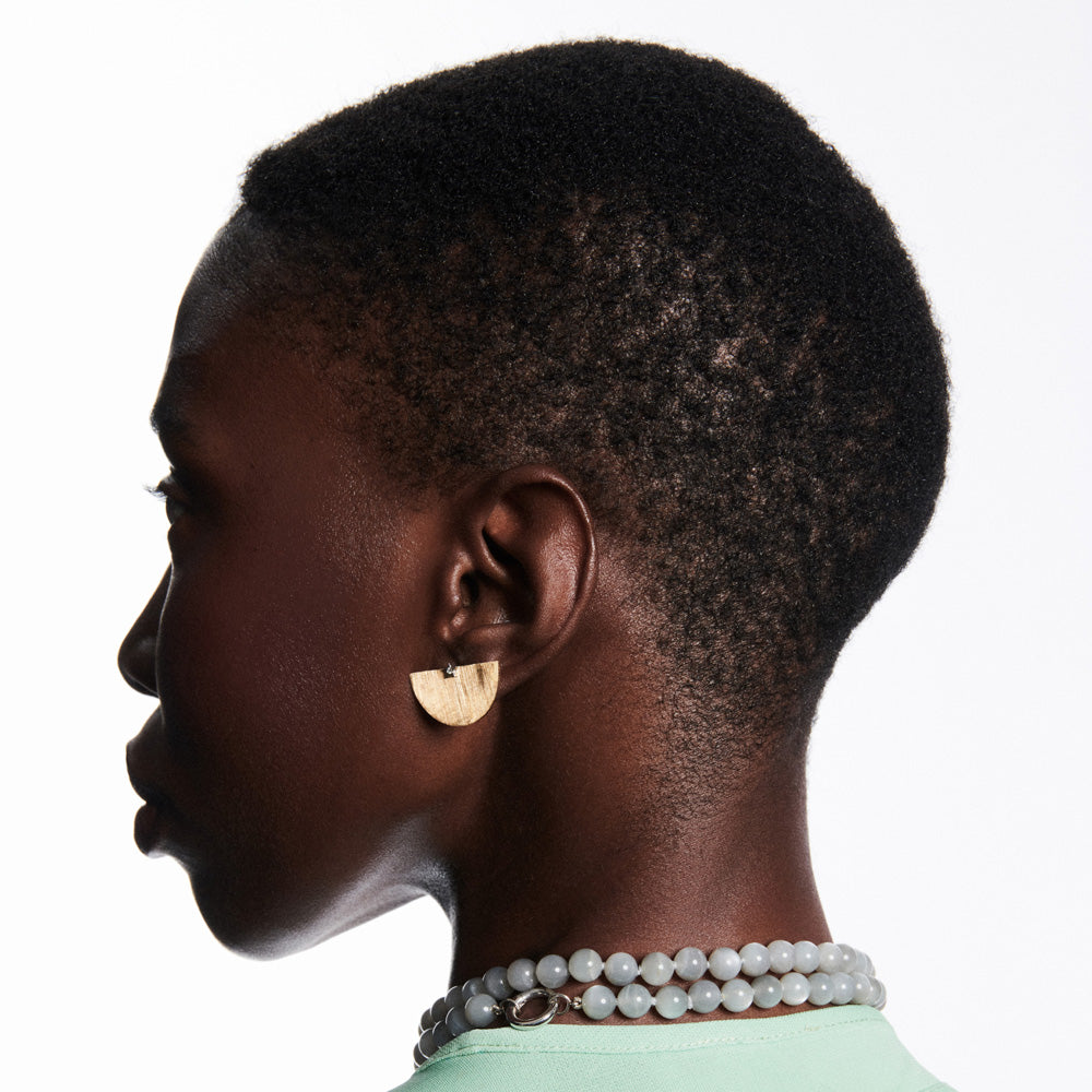A black woman with a short afro wearing push back earrings and a necklace adorned with Anna Maccieri Rossi's Ora Half an Hour Earrings, made of white gold and diamonds.