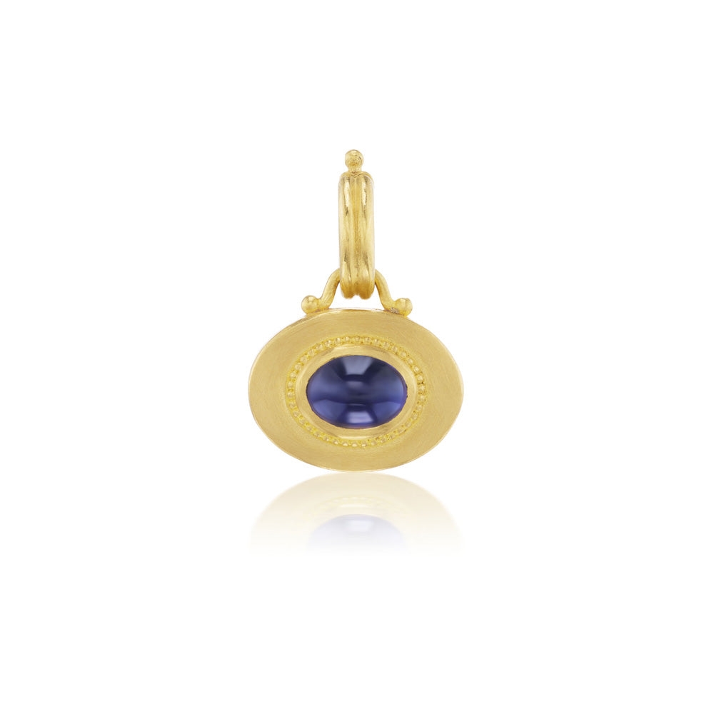 A yellow gold pendant with a blue sapphire stone and a Prounis Granulated Heart Charm on the chain.