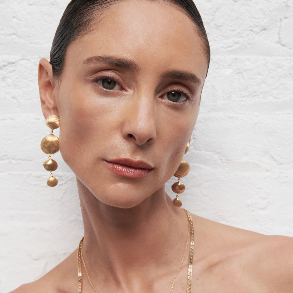 A woman wearing Cadar's Four Shell Drop Earrings and necklace made of 18k yellow gold.